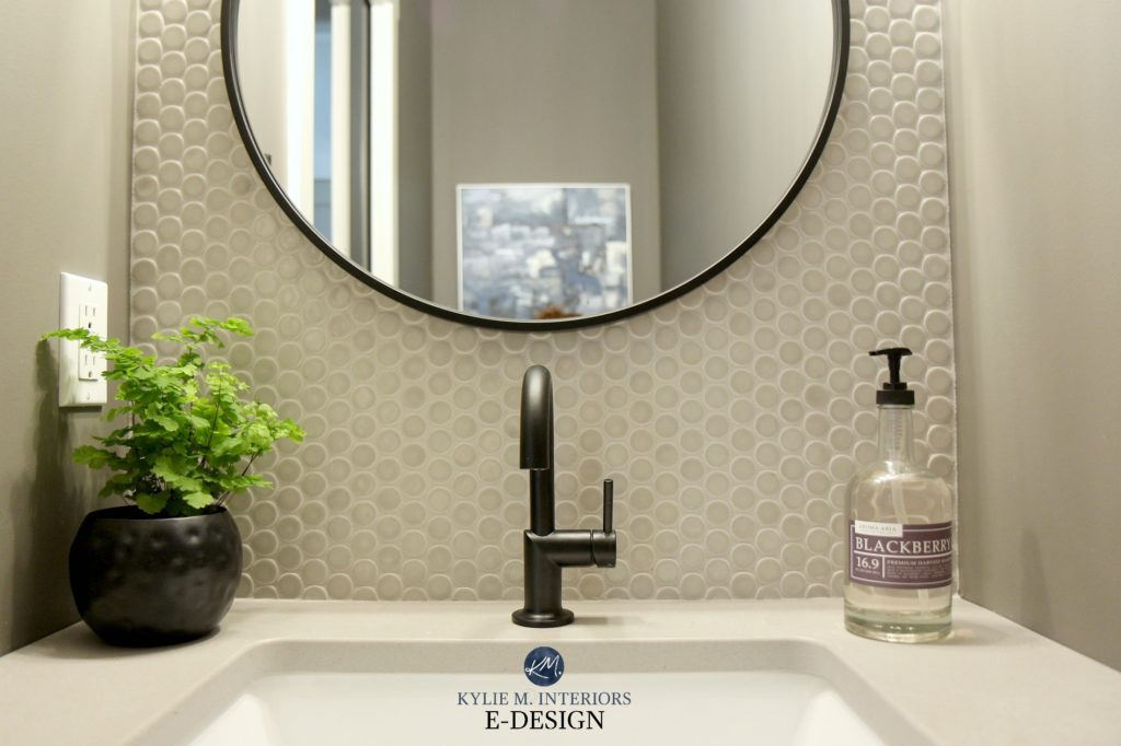 Small powder room bathroom with penny tile accent behind wood vanity, concrete look quartz countertop. Black fixtures and round mirror. Kylie M Edesign