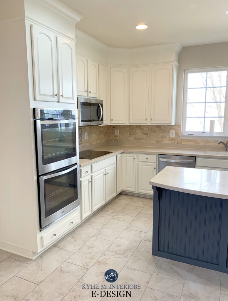 Kylie M Interiors Edesign. Oak cathedral style arched cabinets painted Benjamin Moore Cloud White, travertine tile backsplash, beige countertop, navy blue Ocean Floor island.
