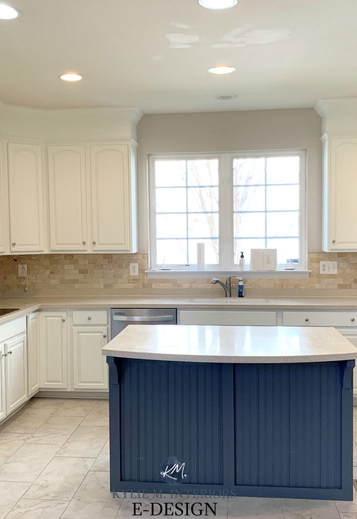 Kylie M Interiors Edesign. Oak cathedral style arched cabinets painted Benjamin Moore Cloud White, travertine tile backsplash, beige countertop, navy blue Ocean Floor island.