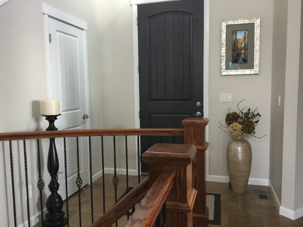 Entryway with front door painted Sherwin Williams Black Fox. Red-toned wood railing and Canvas Tan walls. Popular E-design paint colour consultant, Kylie M