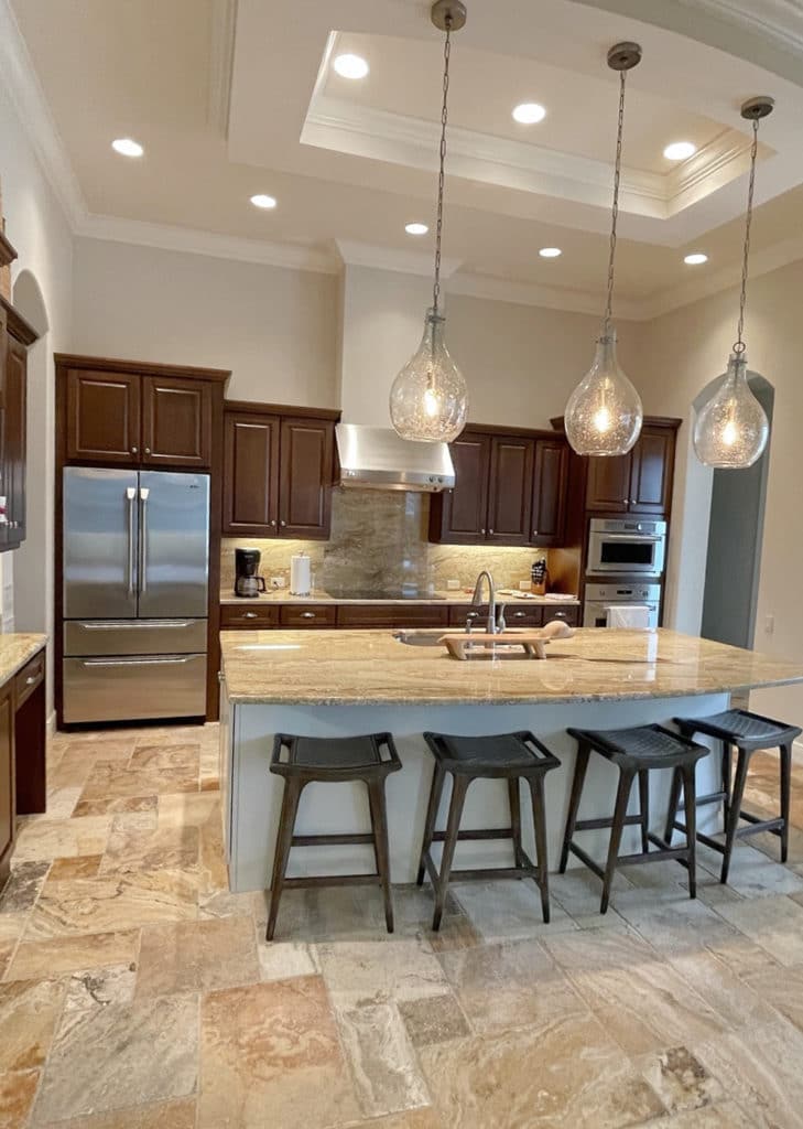 Kitchen with dark wood cabinets, travertine floor, Sherwin Williams Canvas Tan paint colour, island and pendants. Kylie M Interiors Edesign