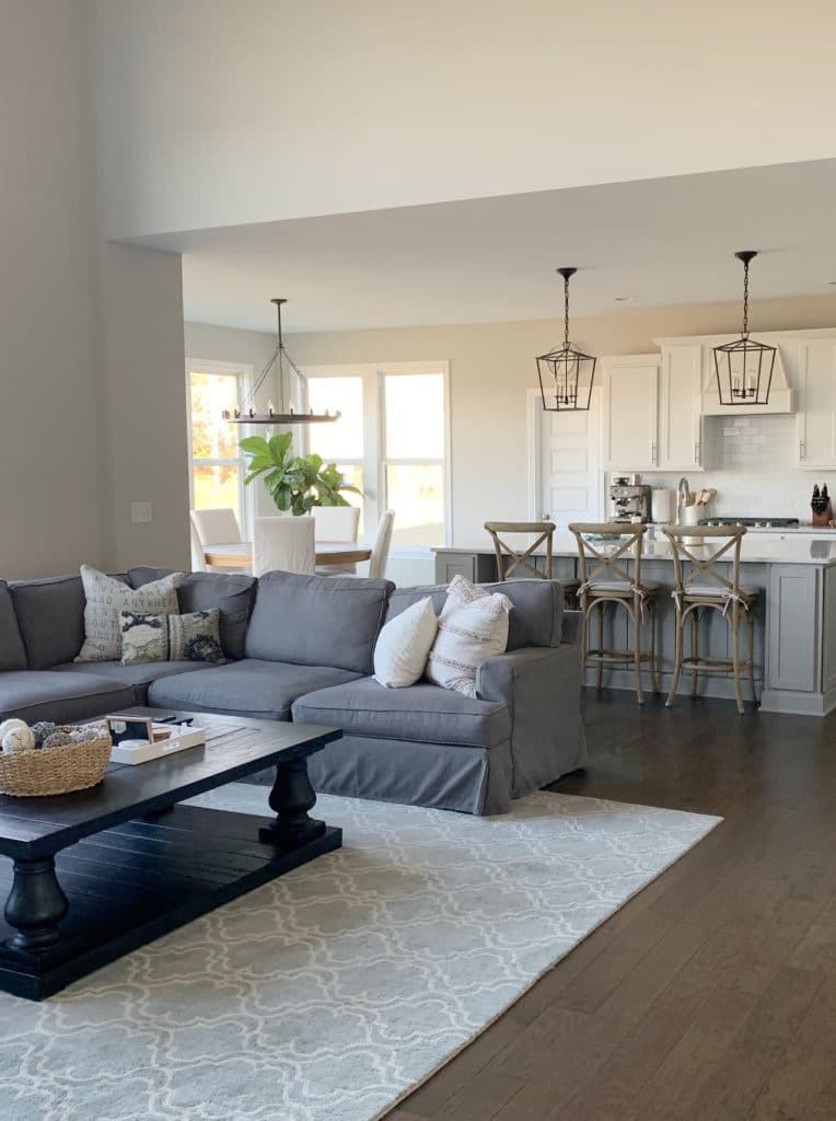Open concept living room and kitchen, Sherwin Williams Agreeable Gray, grey sectional. White cabinets. Kylie M Interiors Edesign, client befor ephoto