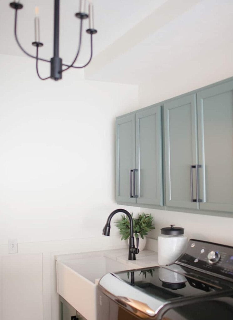 Modern farmhouse style luandry room with Benjamin Moore Caldwell Green paitned cabinets, farmhouse sink with white quartz and black faucet, Pure White walls