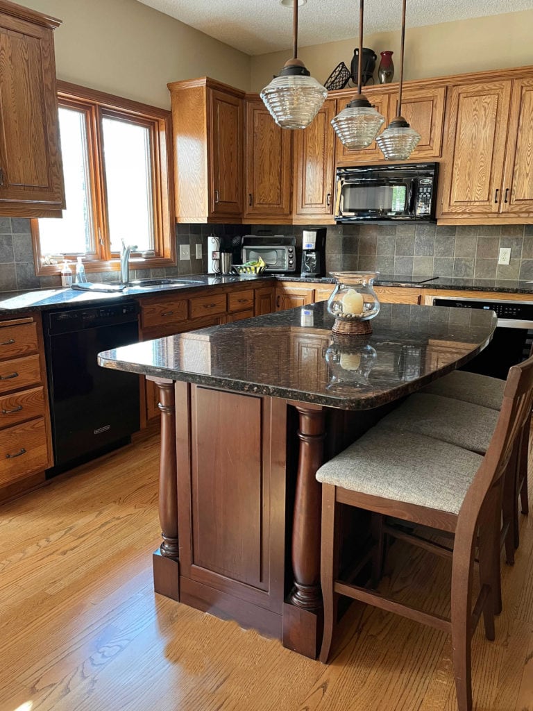 Oak cabinets orange hue, wood floor, red cherry wood island, black granite, Putnam Ivory beige paint color on walls.