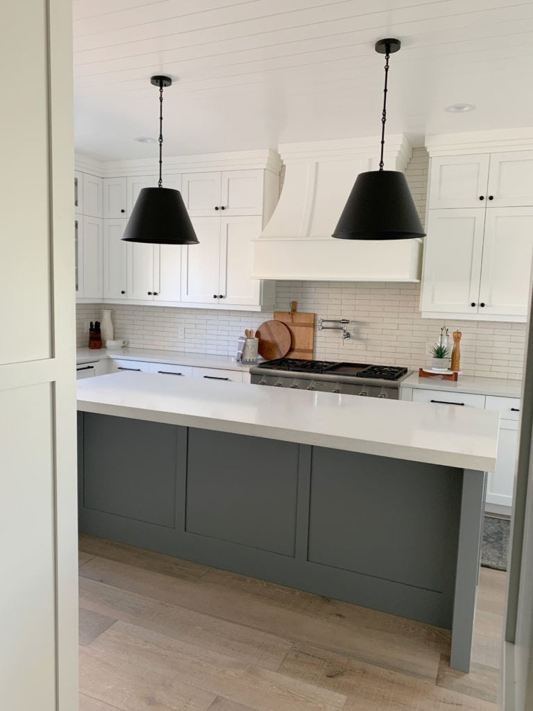 Sherwin Williams High Reflective White cabinets with Magnolia Teak Cups on the island, whitewash wood floor, black pendants and white quartz