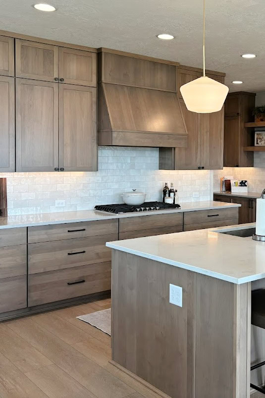 Alder Oasis stained wood kitchen cabinets, wood island, quartz Sandstone and Enigma countertop, wood floor light gray wash, subway tile backsplash, gold pendant lights