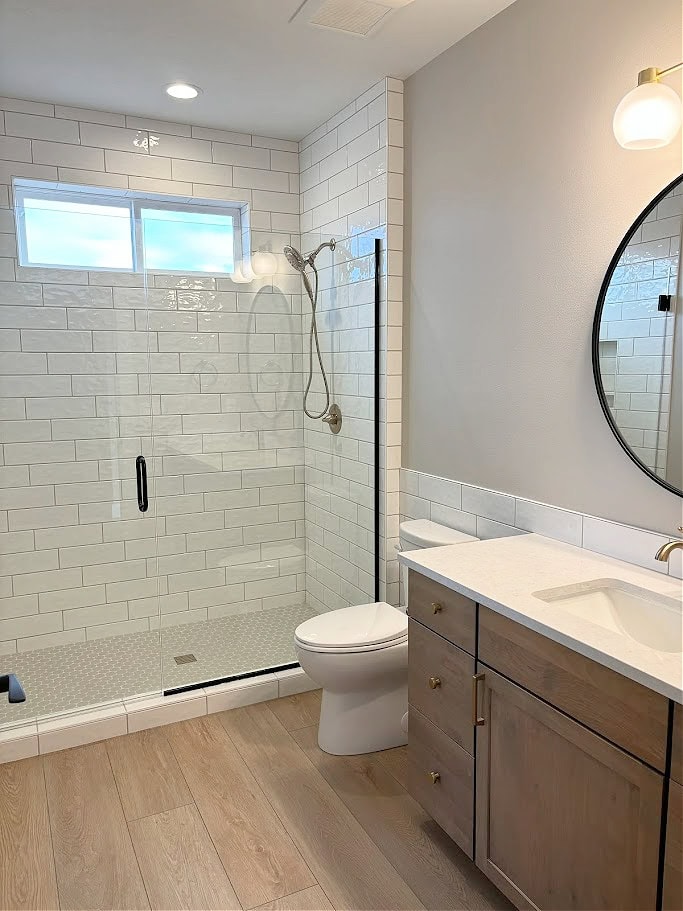 Bathroom with wood look tile floor, maple stained wood vanity, white quartz countertop, subway tile, shower floor accent tile, Sherwin Williams Agreeable Gray walls, gold brass faucet