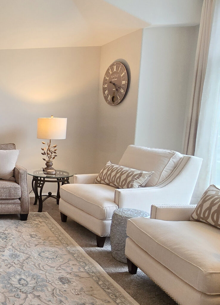 Benjamin Moore Winds Breath in living room with light beige accent chairs, taupe warm gray carpet on area rug