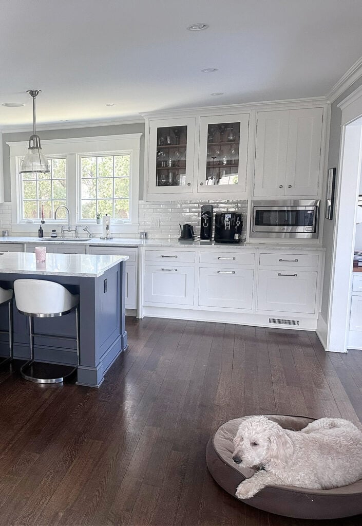 Bright cool white kitchen cabinets, glass front, blue gray painted island, dark wood floor, marble countertop, chrome hardware