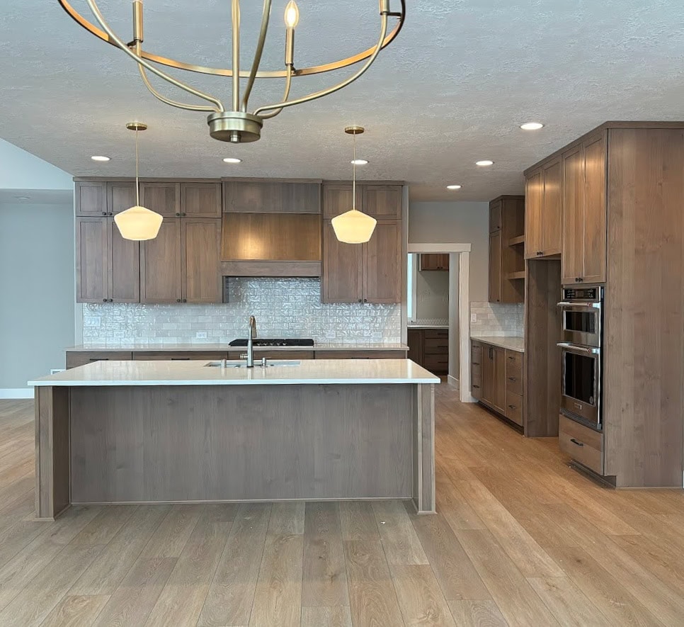 Kitchen with gold brass pendant lights, wood stained island, ALDER cabinets SIMILAR TO MAPLE, wood gray wash floor, subway tile backsplash