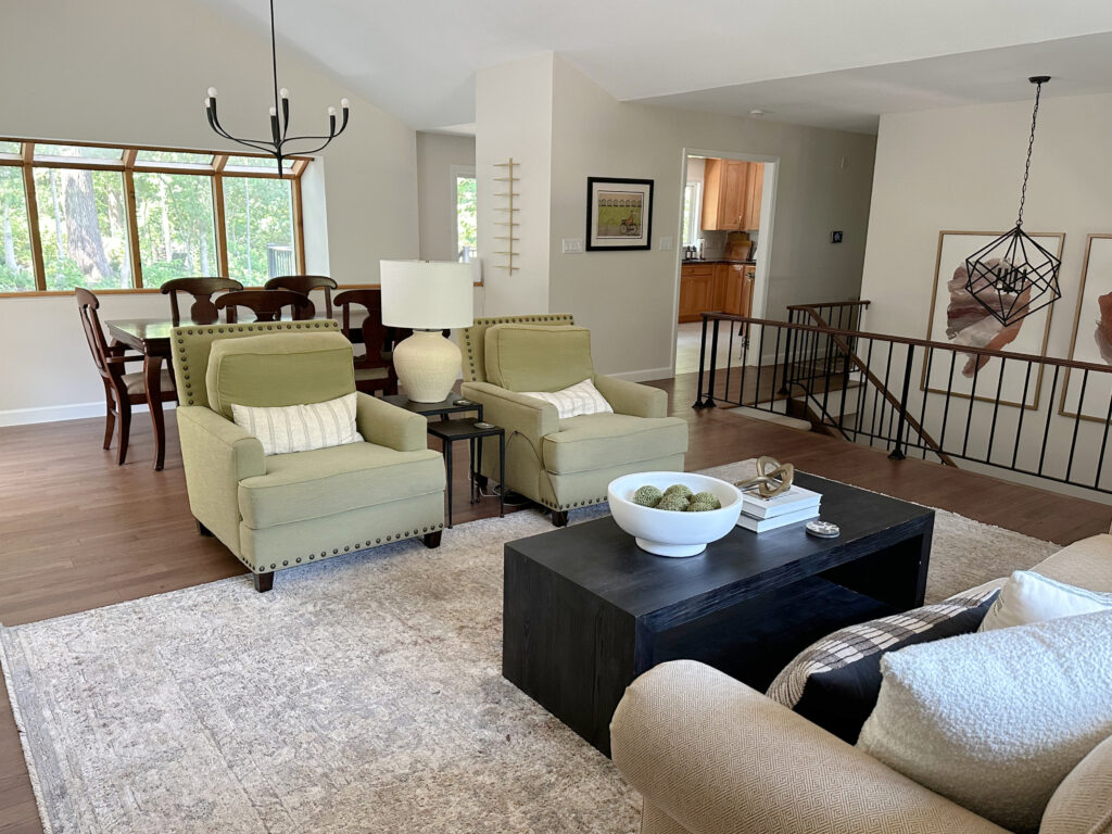 Open concept home and layout in split level home, wood floor, Sherwin Williams White Duck on walls with metal stair railing, vaulted ceiling, green accent chairs