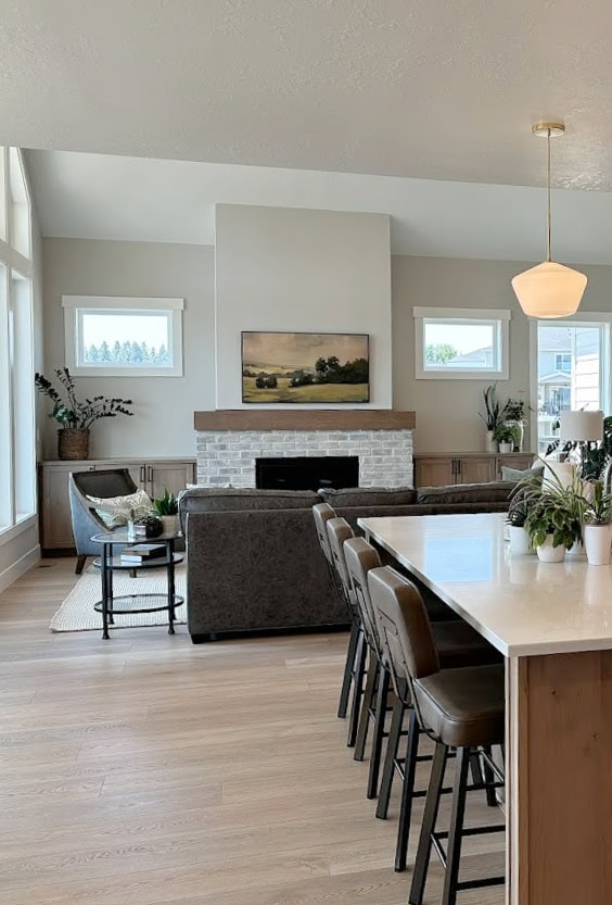 Open concetp living room and kitchen. Wood island, wood gray wash floor, Sherwin Williams Agreeable Gray walls, pure white trim, brick fireplace, vaulted ceiling