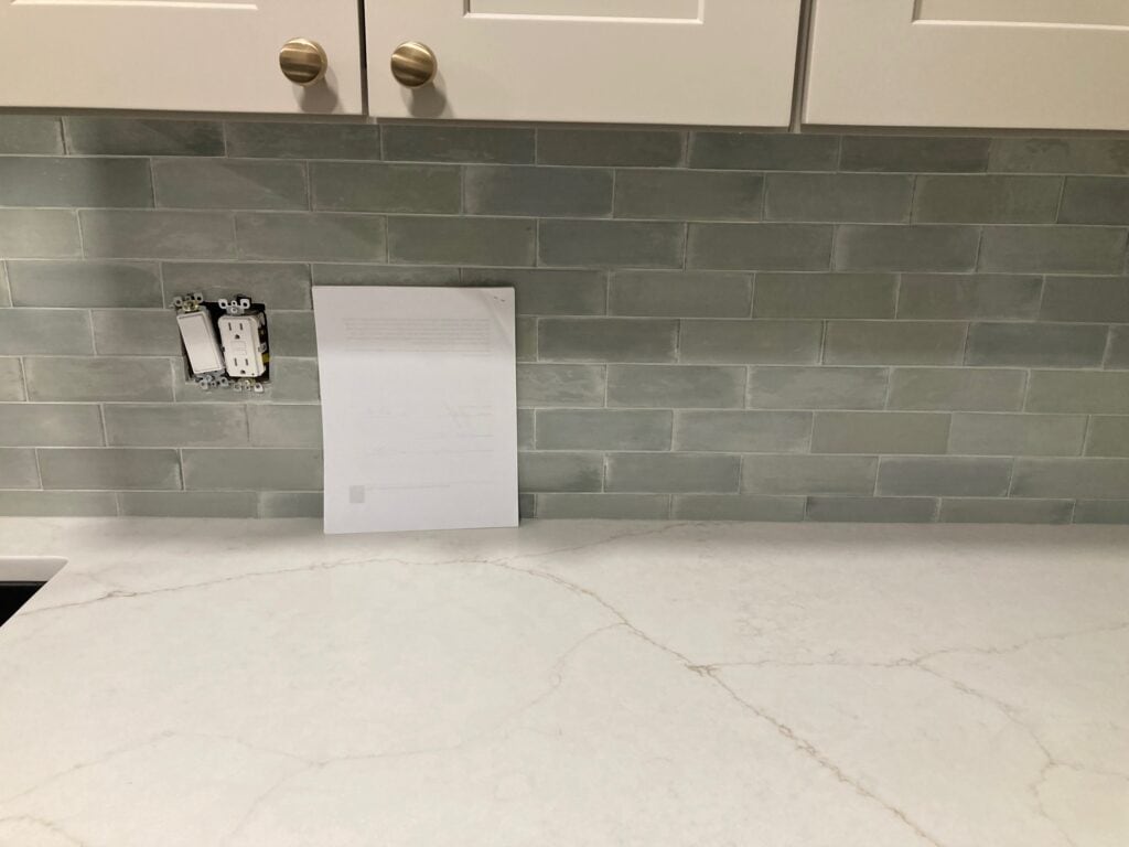 Wellfleet Aquamarine, blue green gray subway tile backsplash with Calacatta Valentin soft off-white quartz countertop with brown veining.