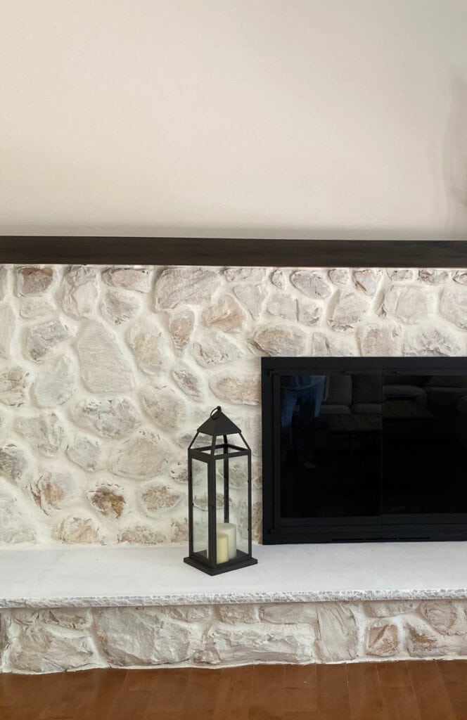 Whitewashed stone fireplace with gas insert, long low mantel, wood floor, warm taupe beige paint color on walls.