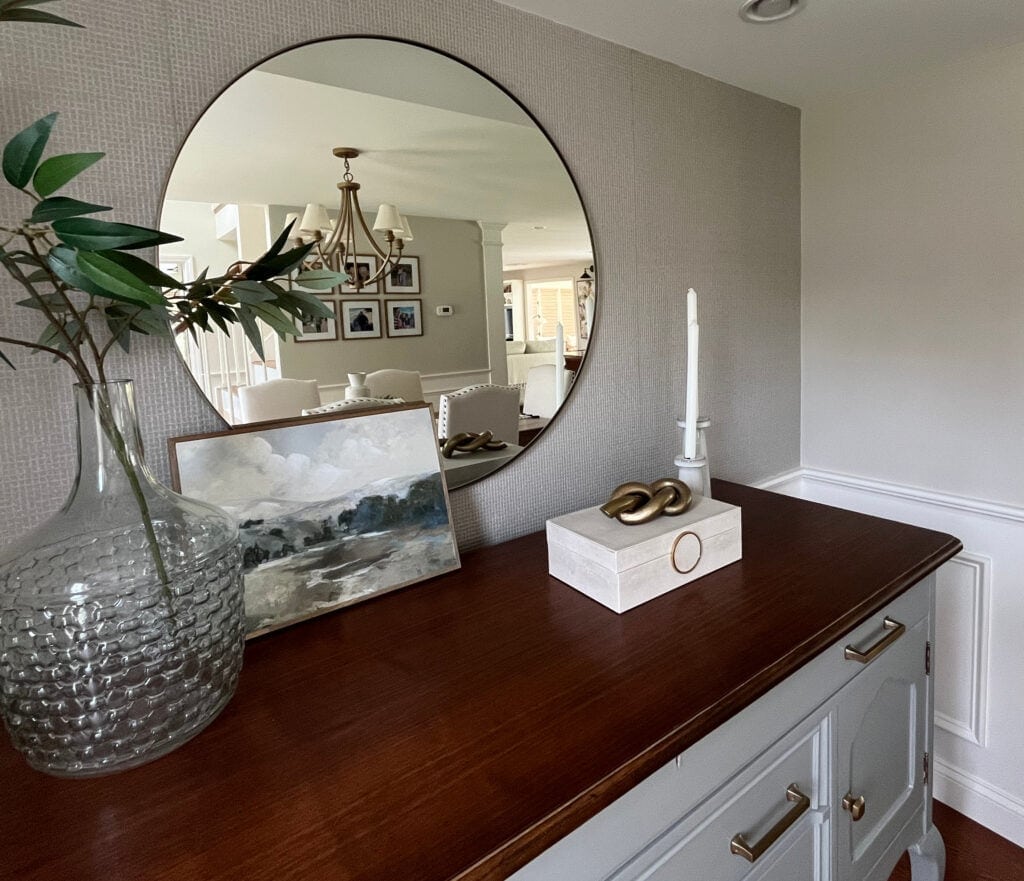 home decor on dining room buffet painted Sherwin Williams Tin Lizzie, Worldly Gray paint color on walls, White Dove wainscoting and trim, round mirror