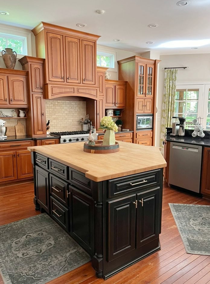 maple or cherry stained red-orange wood cabinets, black kitchen island, wood floor, travertine backslash, black granite countertop, butcherblock island, ideas to update 2000s kitchen