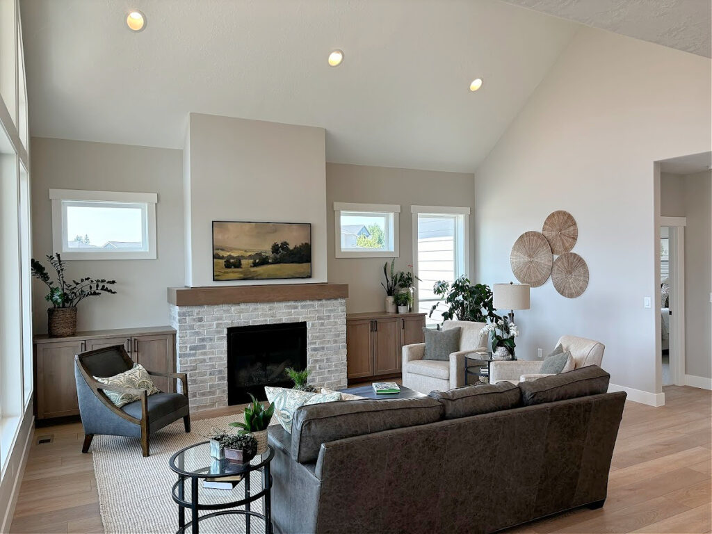 open concept living room furniture layout, brick fireplace, vaulted ceiling, Sherwin Williams Agreeable Gray paint color on walls, Pure White trim, wood floor, wood mantel, home decor
