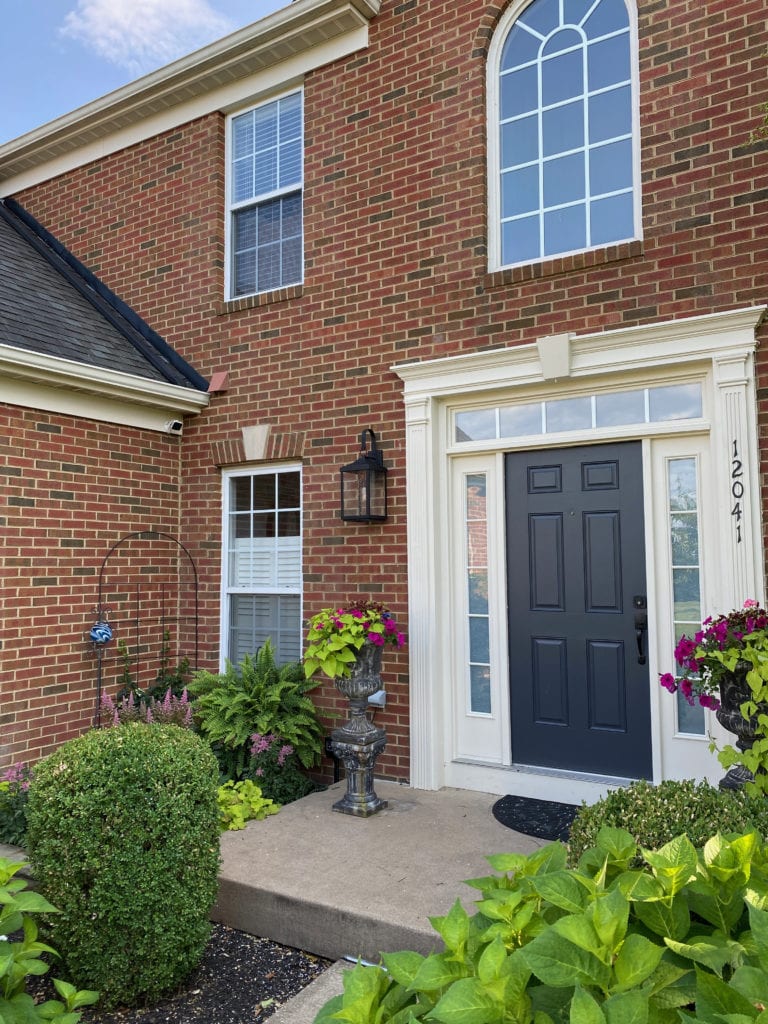 Front door of home with red brick exterior. Charcoal dark gray black roof. Cream trim, Benjamin Moore Wrought Iron front door. Kylie M Interiors Edesign, update ideas