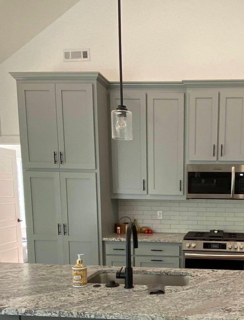 Sherwin Williams Cityscape painted gray green-blue kitchen cabinest with granite countertop, stainless steel appliances, white subway tile
