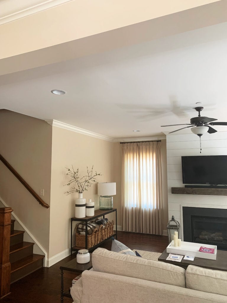 Sherwin Williams Kilim Beige, living room with darker red toned wood flooring, shiplap fireplace, beige sofa, cream trim.
