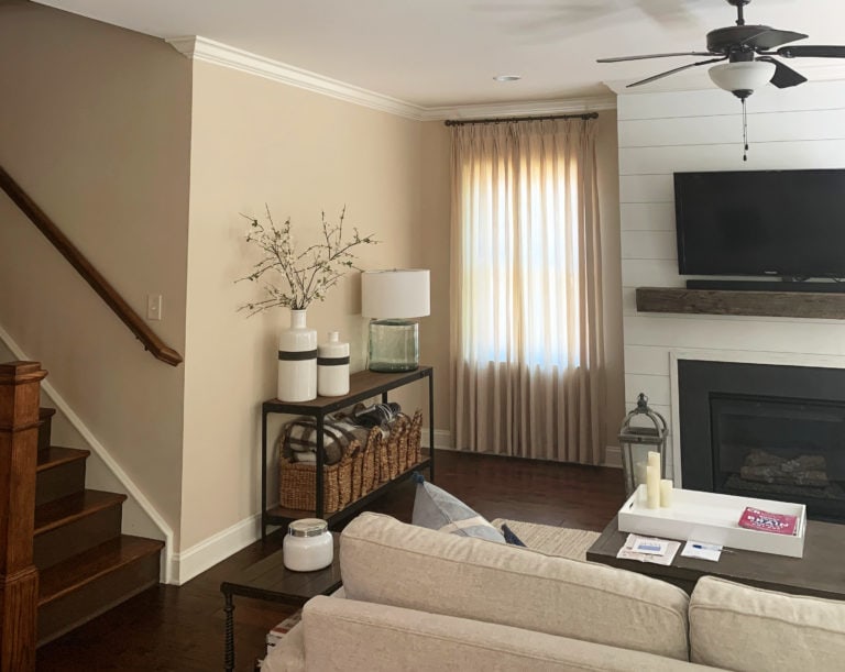 Sherwin Williams Kilim Beige, popular warm neutral paint colour. Family room with fireplace, shiplap, dark red hue wood flooring. Beige sofa