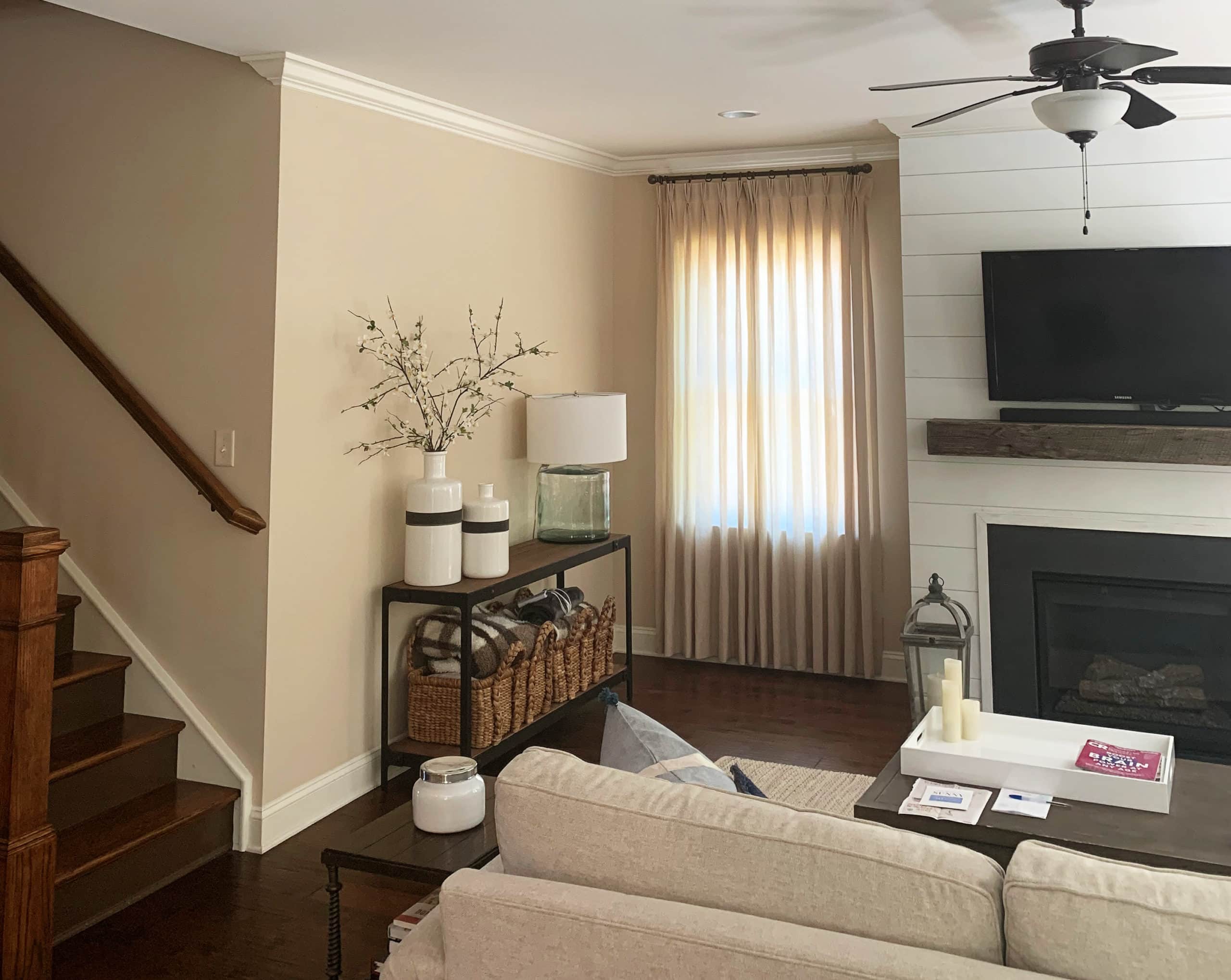 Sherwin Williams Kilim Beige, popular warm neutral paint colour. Family room with fireplace, shiplap, dark red hue wood flooring. Beige sofa