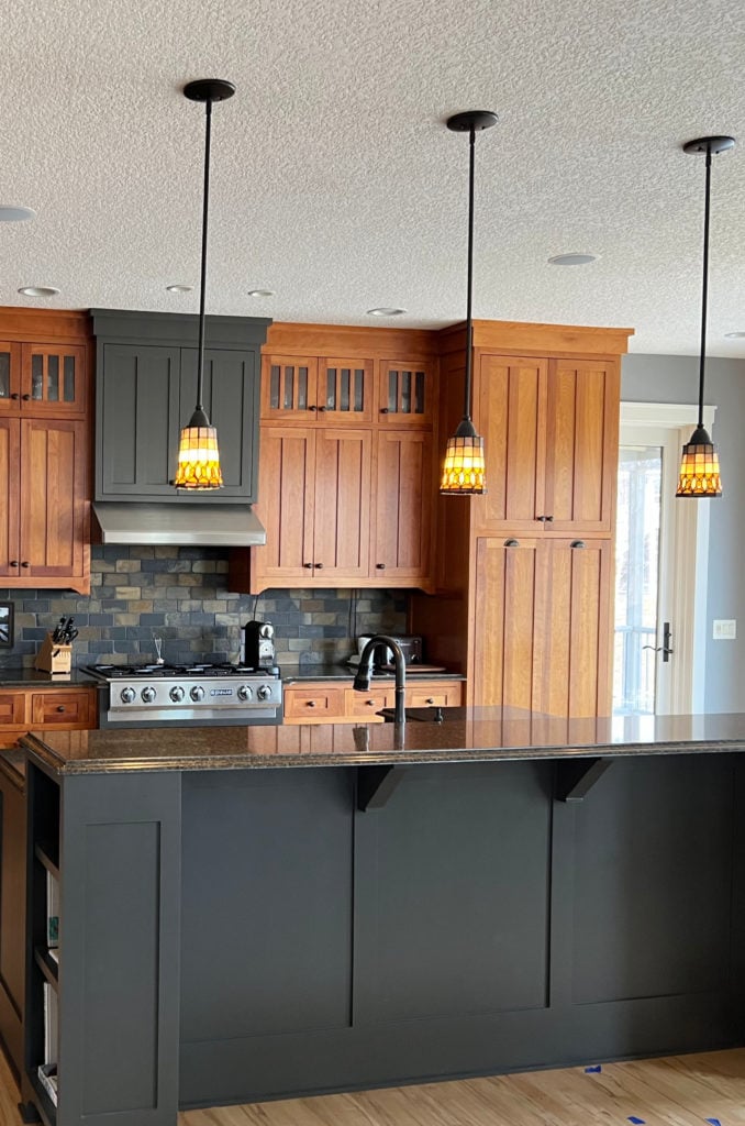 Cherry cabinets with island painted dark gray green, light wood flooring, slate tile backsplash, black granite countertop. Kylie M INteriors Edesign