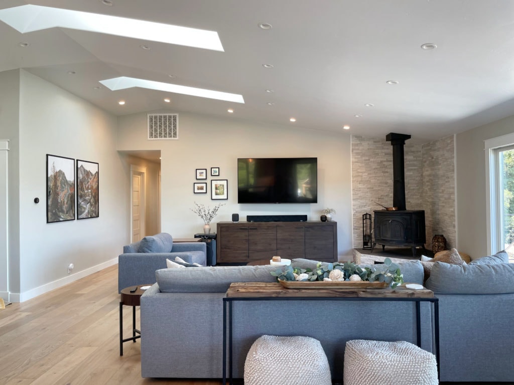 Open concept great room, living room, wood burning stove, stone fireplace, Sherwin Williams Repose Gray warm gray paint color on walls, gray sectional, light wood floor. Kylie M.