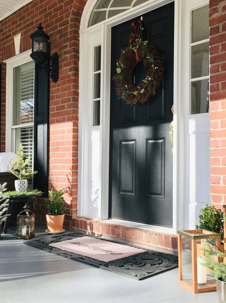 Black front door with red orange brick exterior, white trim, gray front porch, christmas decor.