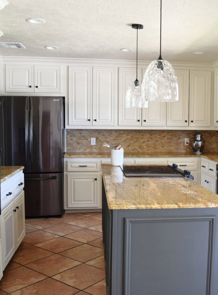 Black stainless appliances, off-white beige painted wood cabinets, Moderate White. orange tile floor, travertine. Kylie M Edesign