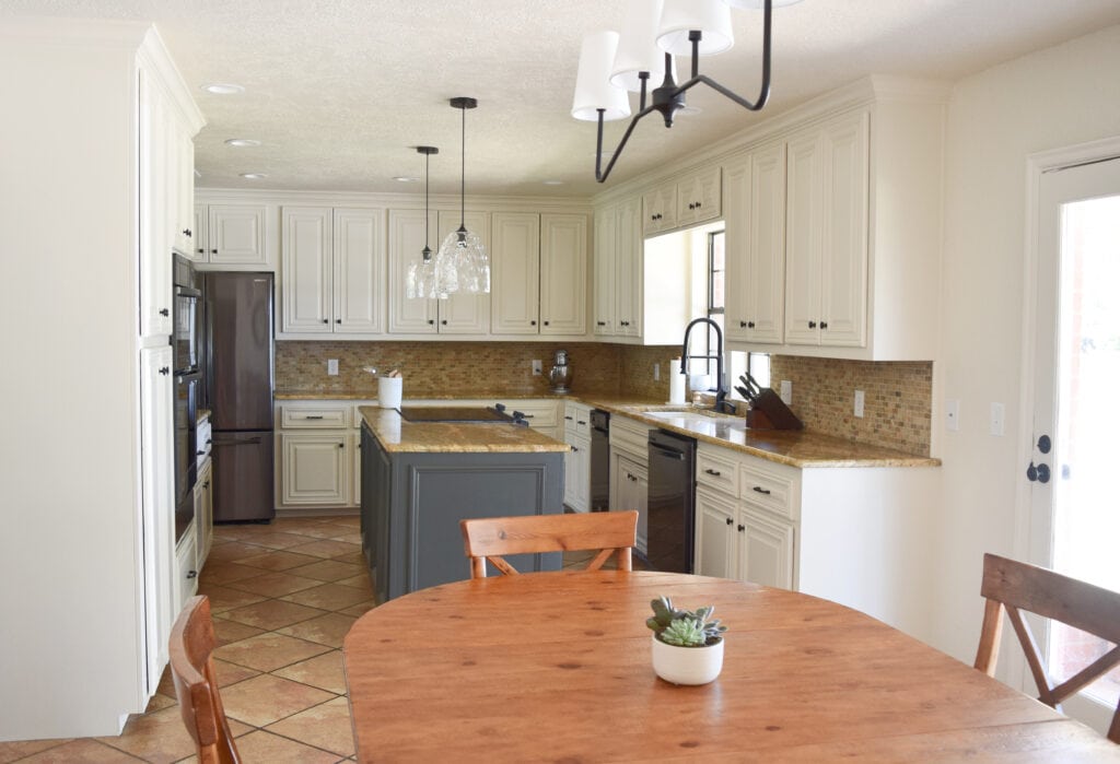 Kitchen remodel painted wood maple cabinets and island, Sherwin Williams Moderate White, travertine, orange tile floor, granite countertop, black stainless steel appliances. Ashwood Moss. Kylie M