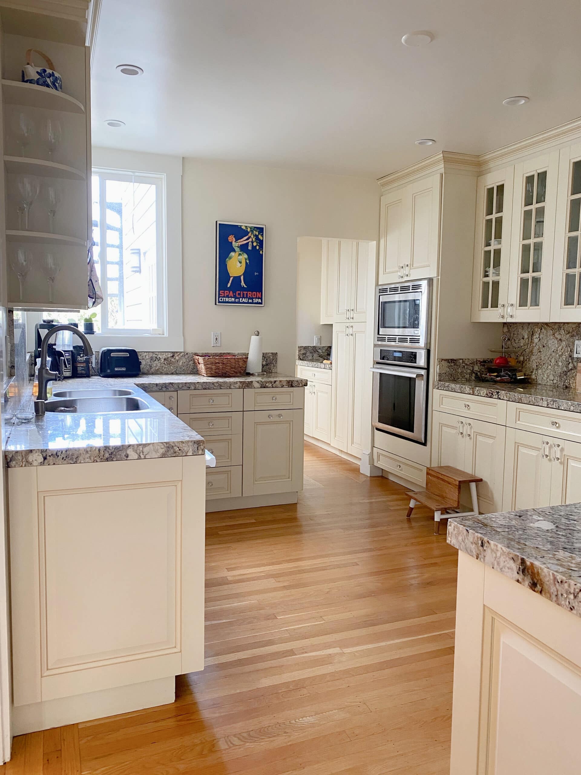 Cream painted kitchen cabinets, warm granite countertop, cream walls, wood floor. Kylie M Interiors online consulting, client photo