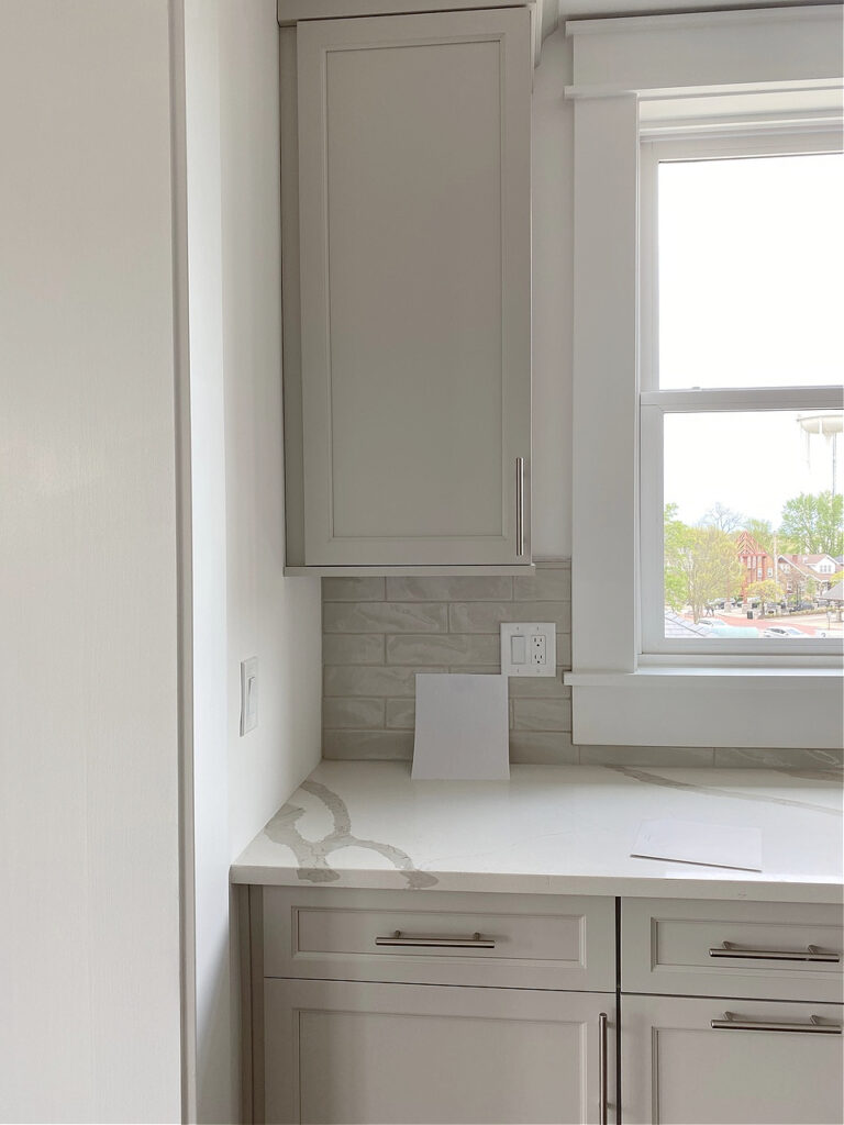 Sherwin Williams Agreeable Gray painted cabinets, nickel hardware, white quartz countertop, subway tile backsplash.