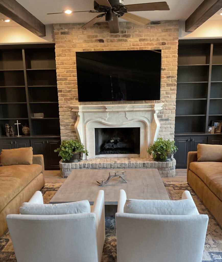 Beige brick fireplace with stone or plaster fireplace surround. Iron Ore painted black built-ins with grass cloth, wood beams on ceiling. Kylie M Interiors Edesign, online paint colors