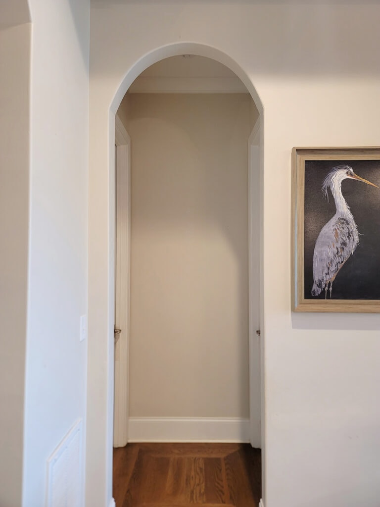 Benjamin Moore Winds Breath match Sherwin. Hallway with arch and wood floor.