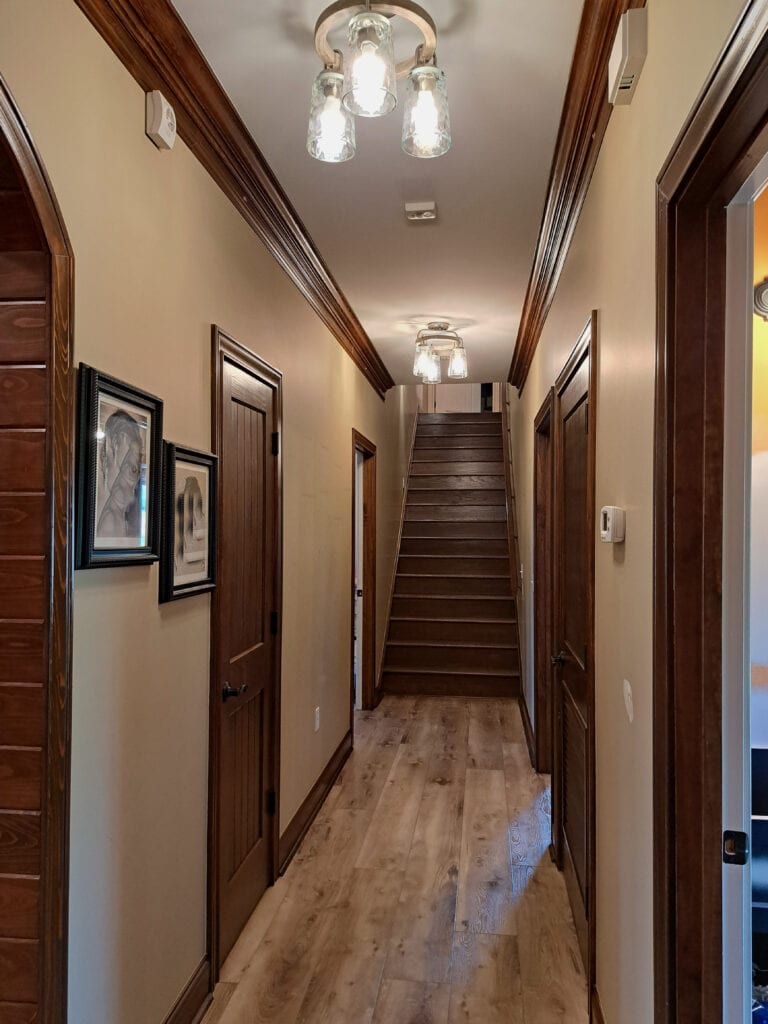 Dark wood trim in dark hallway with Sherwin Williams Basket Beige and wood stairs. Client photo, Kylie M Interiors Edesign