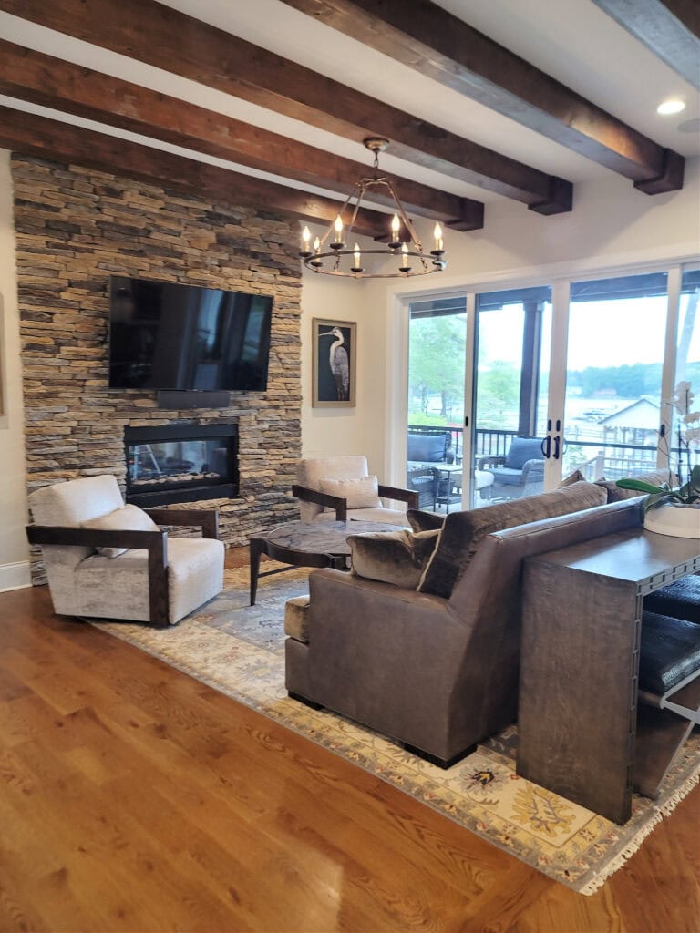 Living room, stone fireplace, dark wood beams on ceiling, wood floor, Benjamin Moore Winds Breath match paint color on walls, south-facing
