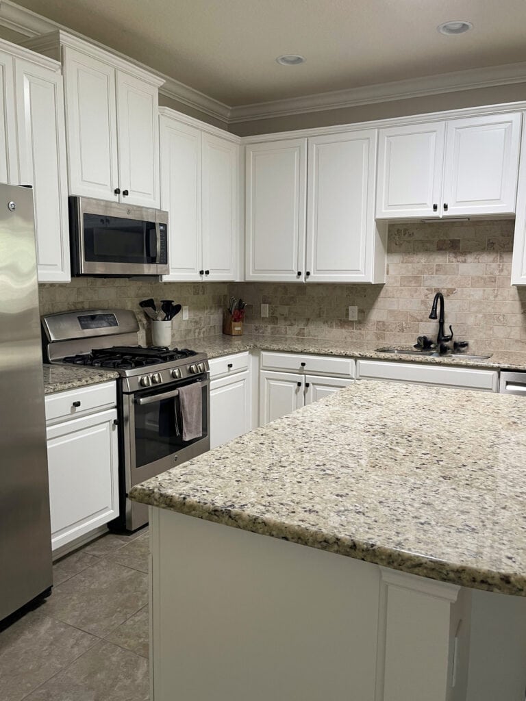 Benjamin Moore warm white cabinets, granite countertop, travertine tile backsplash, beige tile floor, stainless steel appliances, kitchen update ideas with Kylie M