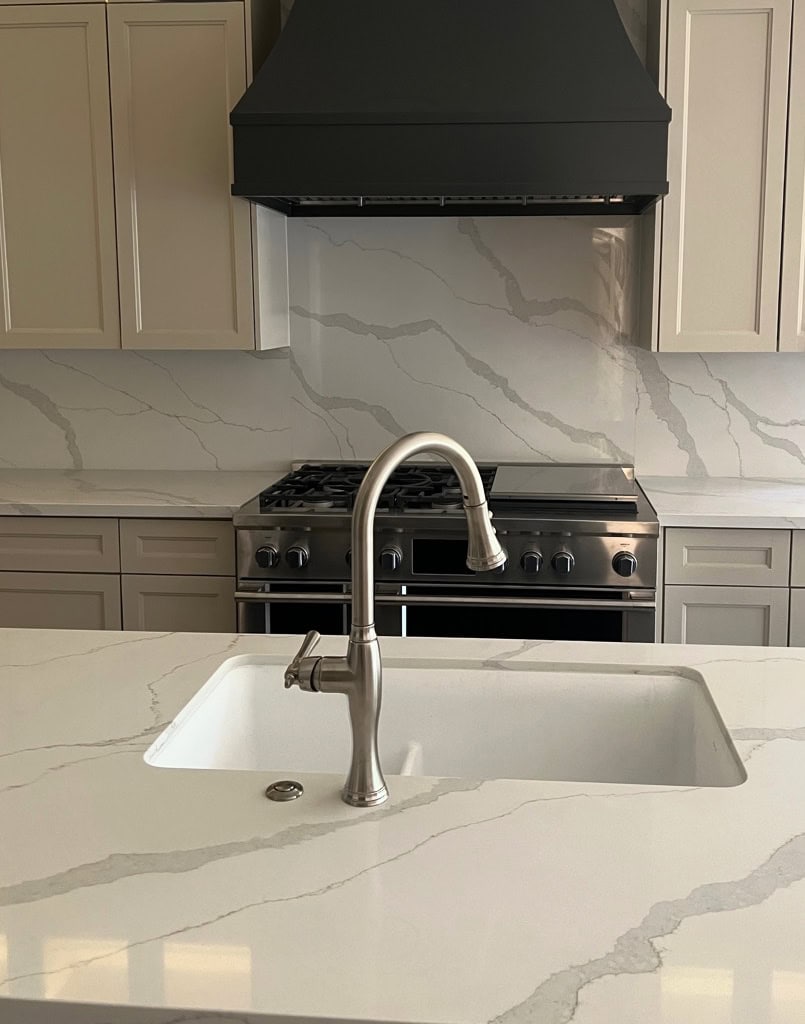 MSI CALACATTA IDILLIO, IRON ORE RANGE HOOD, Sandbar, beige tan painted kitchen cabinets, polished nickel faucet. Same quartz countertop on backsplash too