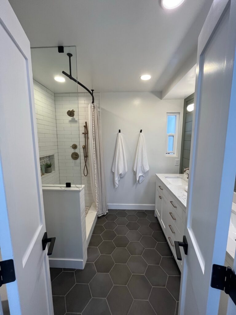 Sherwin Williams Alabaster warm white walls in bathroom, dark gray hexagon tile floor, walk in shower, Evergreen Fog green accent wall behind vanity