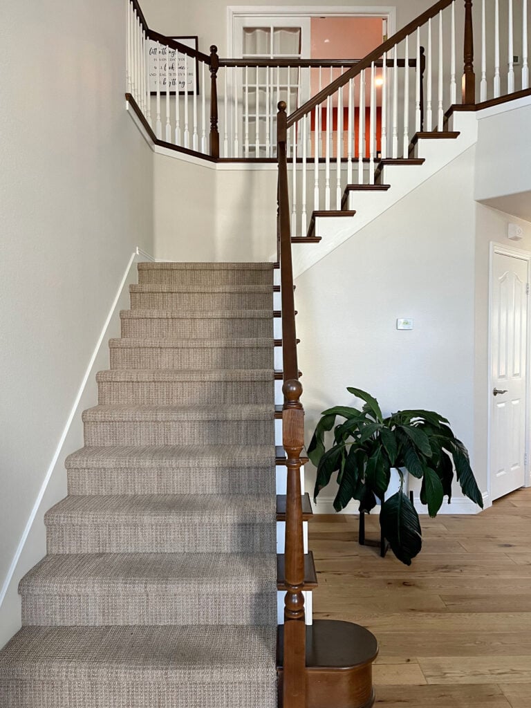 Sherwin Williams Neutral Ground, beige tan carpet on stairs, wood floor, wood hand railing.
