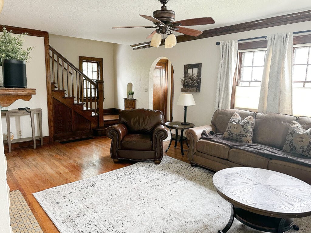 Living room in old, vintage antique home with dark wood trim and stiarcase, oak, wood floor, Benjamin Moore Maritime White beige paint color on walls