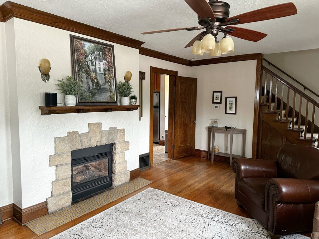 Rustic, old stone fireplace surround, wood mantel, dark wood trim and staircase, wood floor, oak, Benjamin Moore Maritime White beige on walls