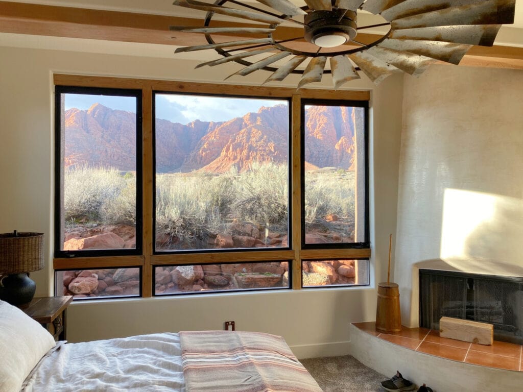 Sherwin Williams Natural Linen best beige paint color, limewash look on stucco rounded corner fireplace, wood beams, desert view bedroom, rustic industrial ceiling fan