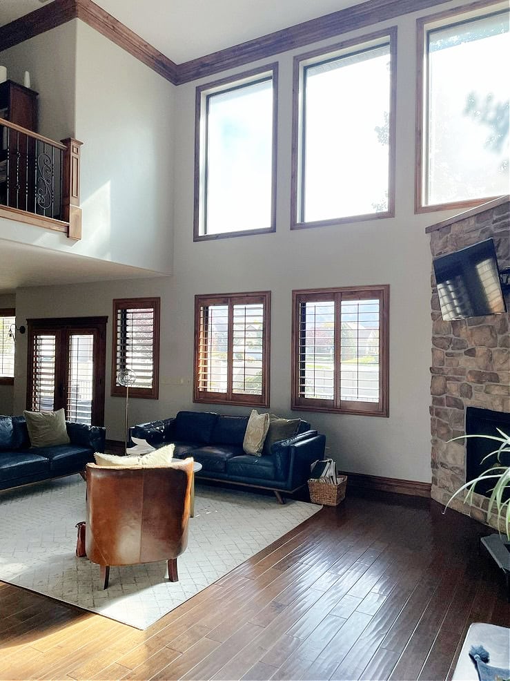 Benjamin Moore Revere Pewter, warm gray in two story living room with dark wood trim and flooring, leather sofa, stone fireplace