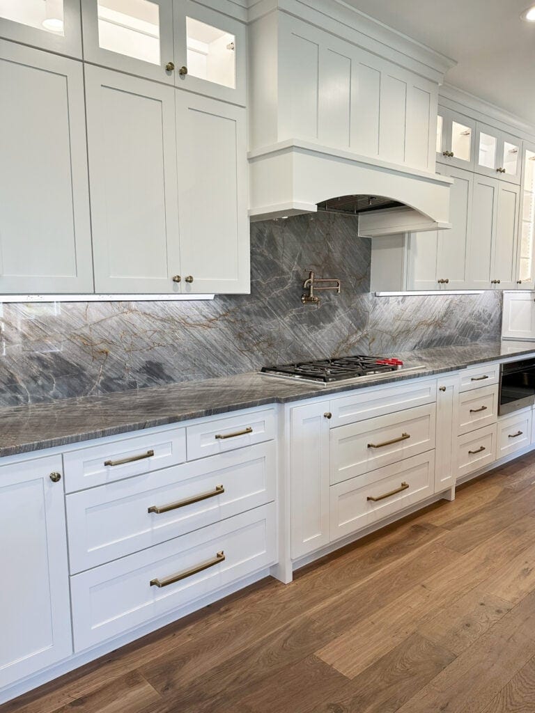 Kitchen cabinets painted Sherwin Williams Pure White, gray, rust quartzite granite countertops, brass hardware, pot filler, range hood. Kylie M Interiors Online c