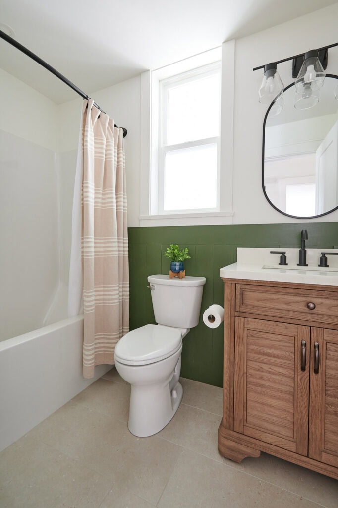 small bathroom with wood vanity, beige tile floor, curved hotel style shower rod and curtain, acrylic bath and shower insert. Dark green Ripe Olive shiplap, White Dove