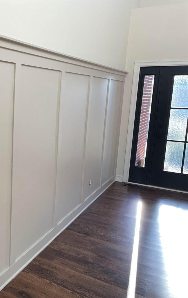 Benjamin Moore Revere Pewter painted board and batten accent in entryway, dark brown oak floor, Chamois off white upper walls White Dove, black front door