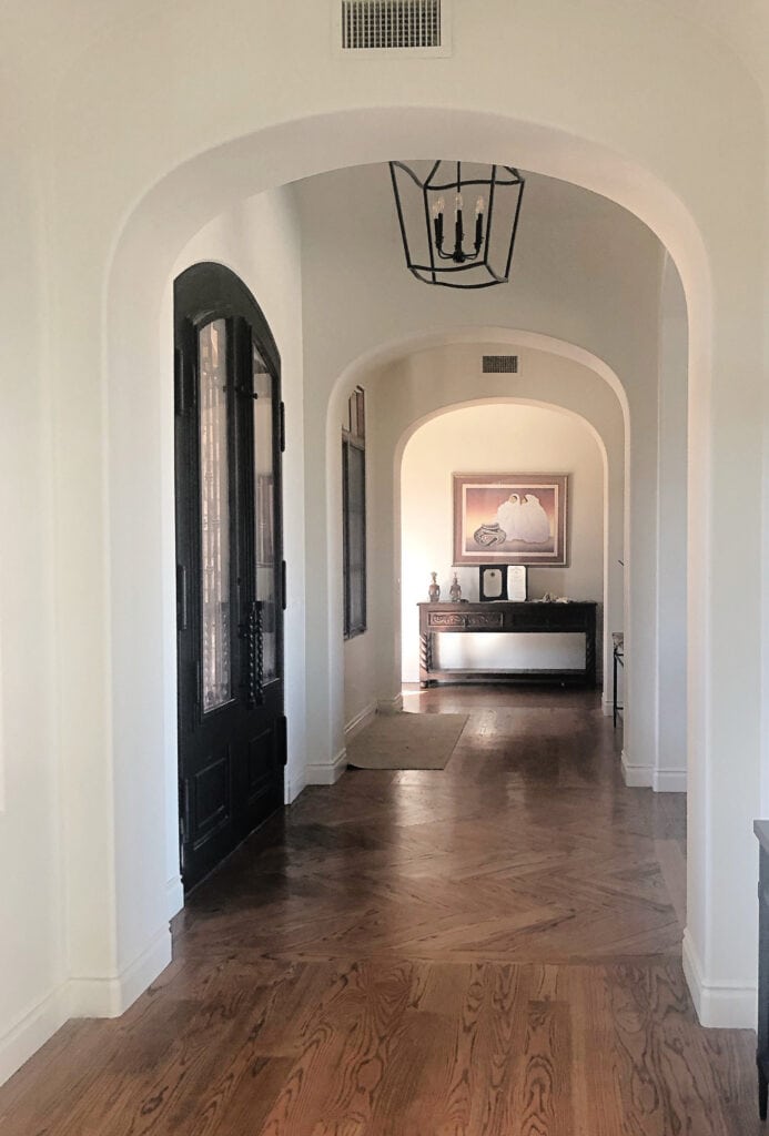 Benjamin Moore Soft Chamois, red toned stained oak wood floor, white trim, hallway with herringbone pattern, archway, arches. Kylie M