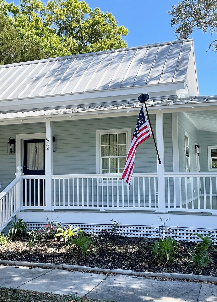 Benjamin Moore White OC 151, painted gray siding with blue undertone, light gray silver metal roof, American Flag, Sherwin Williams Still Water front door